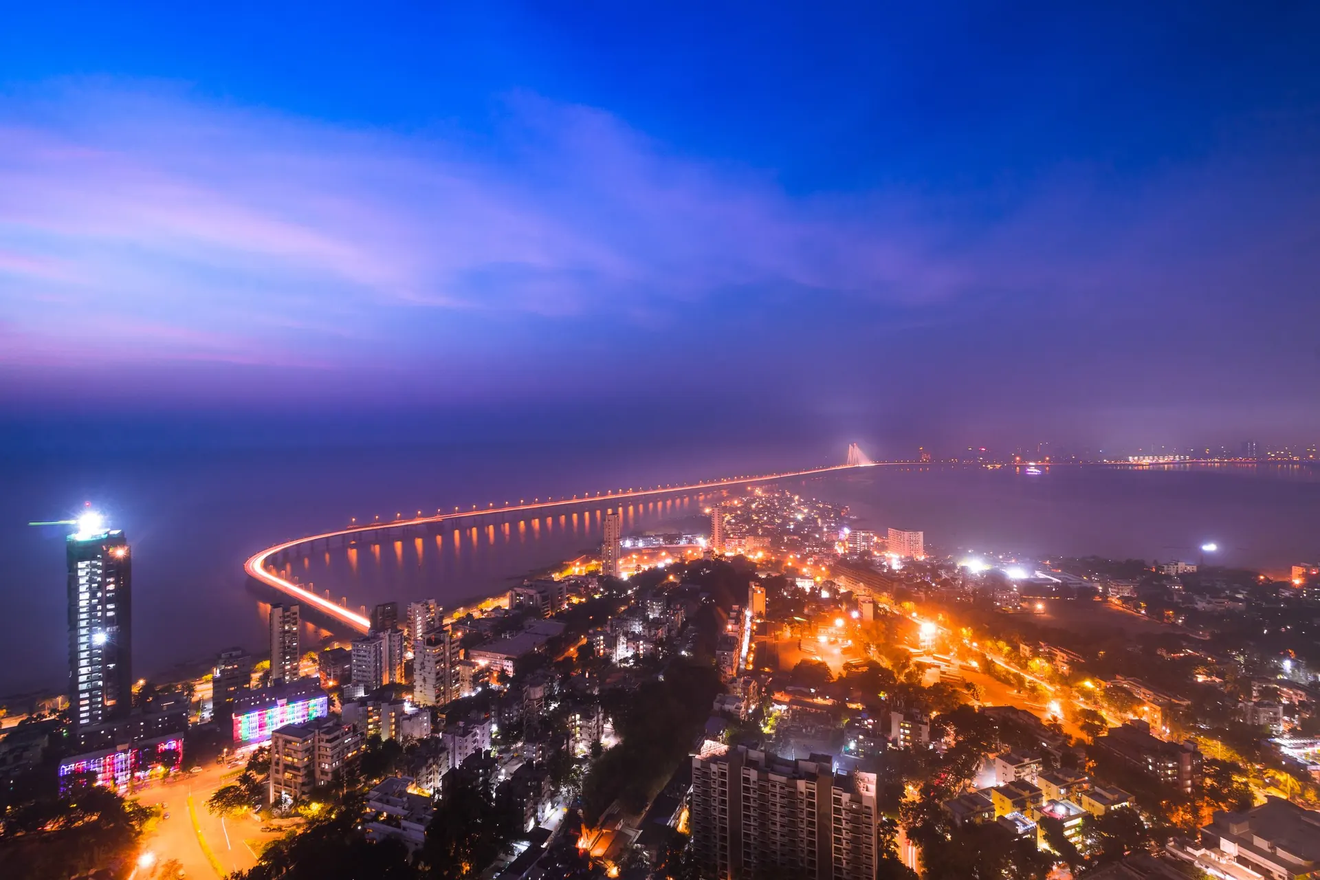 The Bandra–Worli Sea Link lit up across the Arabian Sea at night, with the Mumbai coastline behind it